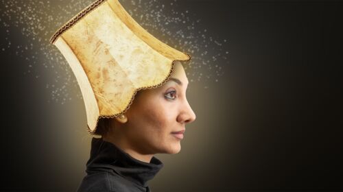Eine junge Frau im Profil hat einen beigen Lampenschirm auf dem Kopf, der strahlt und Funken zu sprühen scheint.
