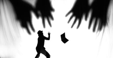Auf diesem Bild sieht man eine Szene aus einem Schattenspiel. Der Schatten eines Menschen hält schützend die Arme nach oben, während große Schattenhände nach ihm greifen. Rechts sieht man den Schatten eines Buches.