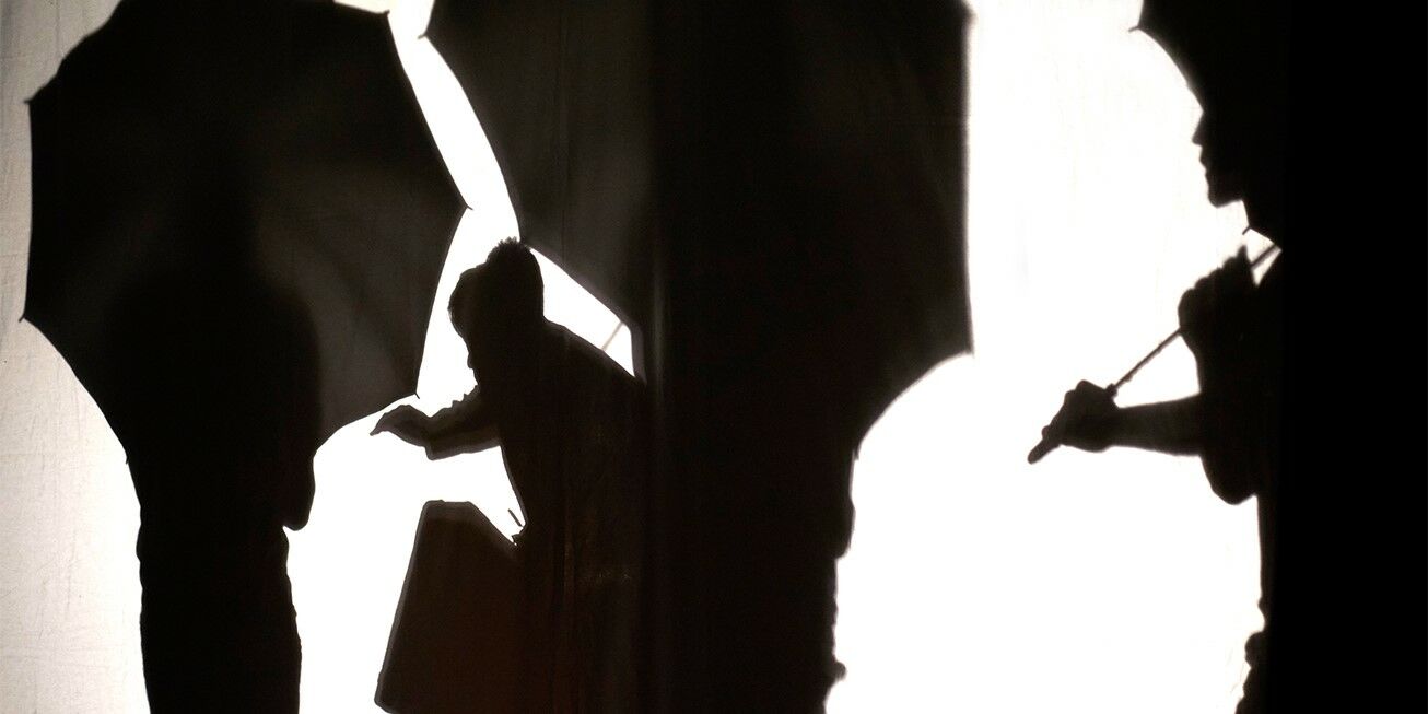 Hier sieht man auf einer weißen Leinwand drei Schatten die jeweils einen Schirm in den Händen halten.