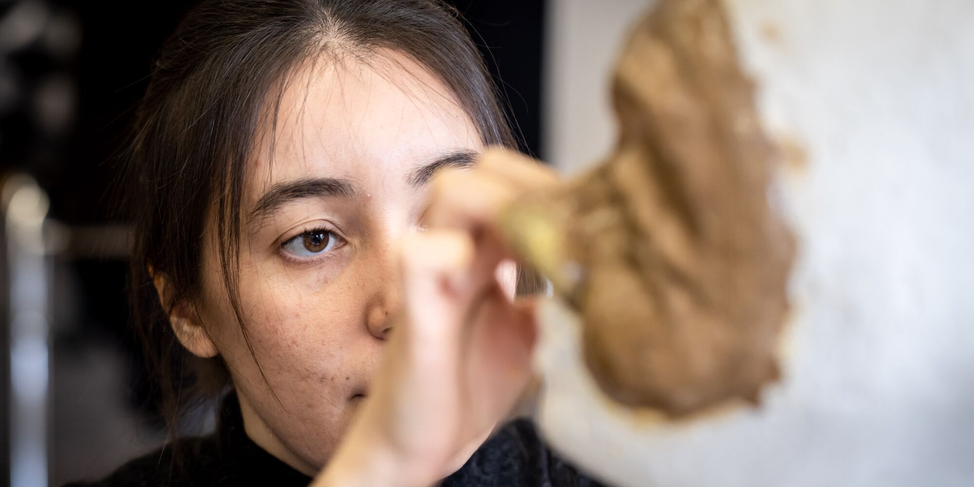 Hier sieht man eine junge Frau, die eine Maske an einen Modellkopf anpasst, der vor ihr steht.