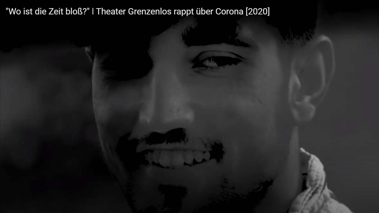 Auf dem Bild sieht man verschwommen einen jungen Mann in schwarz-weiß, der lachend auf die Seite sieht. Es ist ein Ausschnitt des Musikvideos zum Rap "Zeitlos", den das Theater Grenzenlos während der Corona-Pandemie aufnahm.