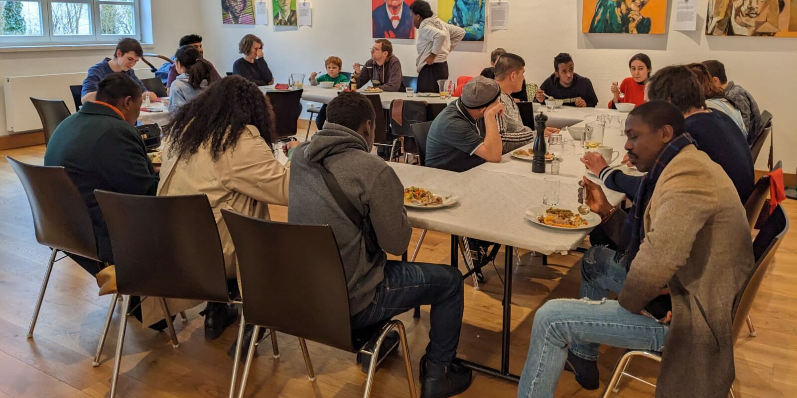 Hier sieht man mehrere Menschen, die an einem langen Tischkreis essen.
