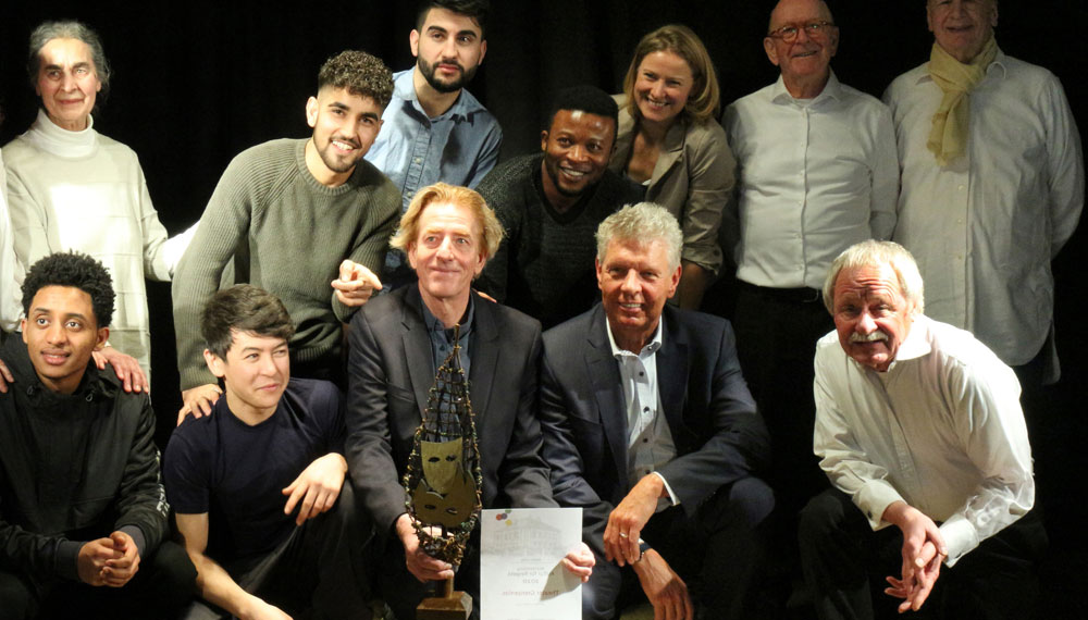 Hier sieht man in zwei Reihen Schauspieler und Schauspielerinnen des Theater Grenzenlos mit OB Reiter und Julia Schmitt-Thiel. Die vordere Reihe kniet und in der Mitte ist der Reggiseur mit einem Preis und der Urkunde in der Hand.