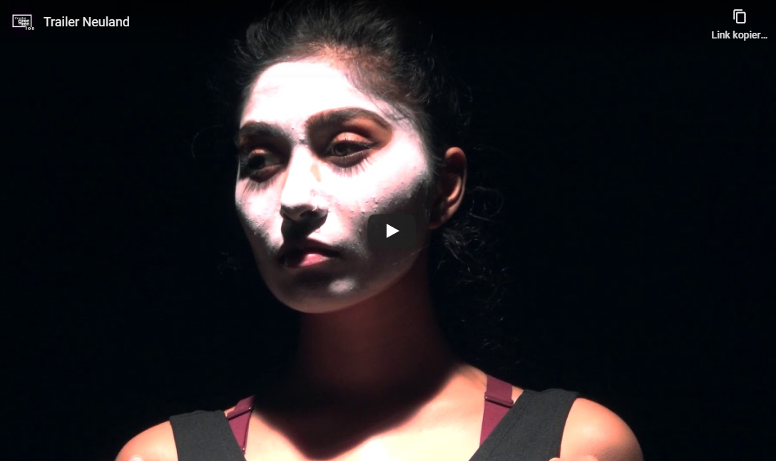 Hier sieht man einen Ausschnitt des Youtube-Videos mit dem Titel "Trailer Neuland", auf dem eine Schauspielerin zu sehen ist, die auf die Seite sieht und weiße Farbe im Gesicht hat.
