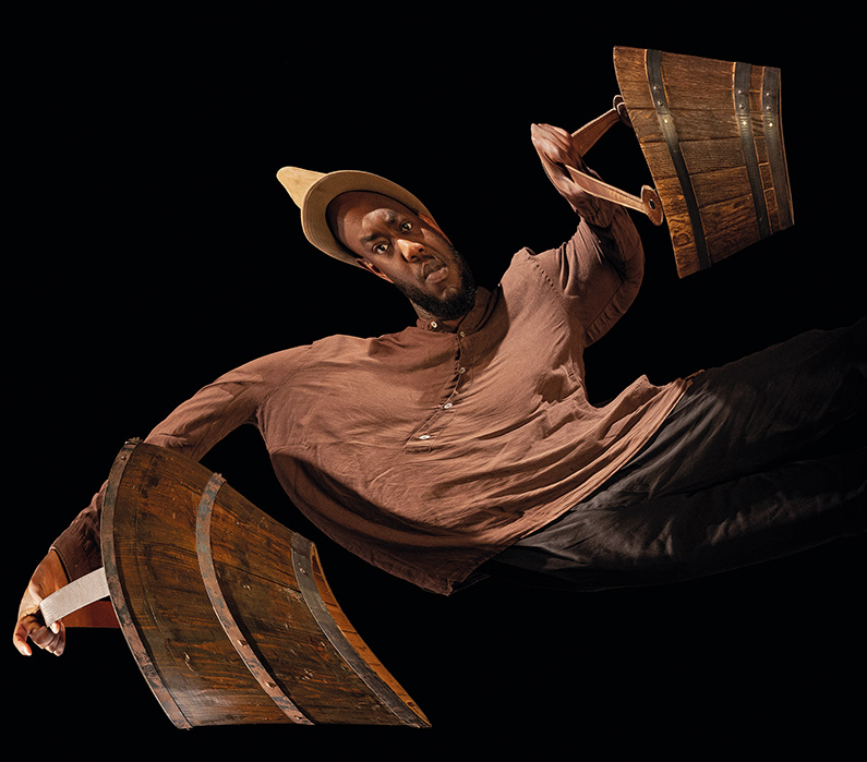 Hier sieht man einen Mann, der zwei schwere Holzkübel trägt. Seine Proportionen sind nachträglich bearbeitet, so dass sein Körper verzerrt wirkt.